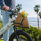 Black front cargo rack on an e-bike, holding a woven bag with flowers, suitable for carrying daily items. 